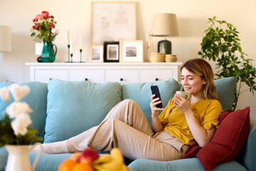 Woman using smartphone and drinking coffee at home in the morning