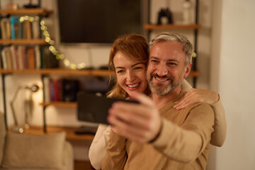 Cheerful mature couple taking selfie with smart phone at home