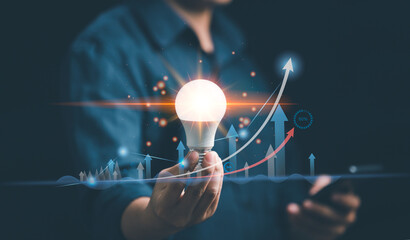 Man hand holding bright light bulb with graph economic