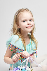 A happy little girl with long blonde hair in a cute turquoise blouse and blue denim shorts on a white