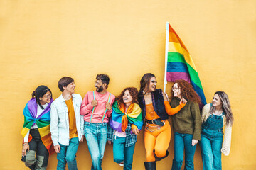 Diverse group of young people celebrating gay pride festival day - Lgbt community concept with guys and girls hugging together outdoors - Multiracial trendy friends standing on a yellow background - obrazy, fototapety, plakaty
