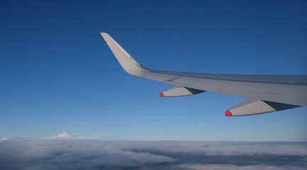 Fototapeta na wymiar Airplane in flight. People travelling. Aerial view from plane window. Blue sky above clouds