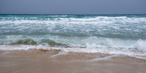 Windy waves crashing on a sandy tropical beach on a stormy day in winter.