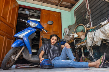 Plakat A young woman is sitting by a motorcycle parked in front of the entrance to a house