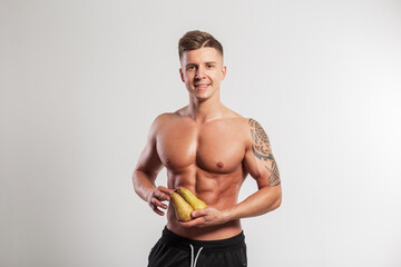 Happy sporty man with smile with hairstyle with muscular body holding pears on white background in studio. Sports and healthy nutrition with vitamins