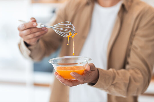 A close-up of a man beating the eggs with a whisk in the kitchen, making breakfast.