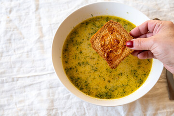 A bowl of soup with a piece of bread being dipped into it