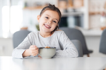 Portrait of a cute little girl with a bowl of cereal and milk for breakfast.