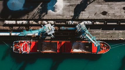 Large harbor cranes unload a ship with fertilizer or rubble in a seaport, aerial view