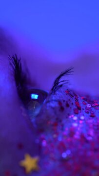Extreme close-up view of female eye with shiny make-up with sparkles. Cinematic macro shot of female eye illuminated pink blue color neon light. Selective focus, part of series. Vertical video shot