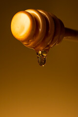 Honey dripping from dipper wooden honey stick macro shot over dark yellow background