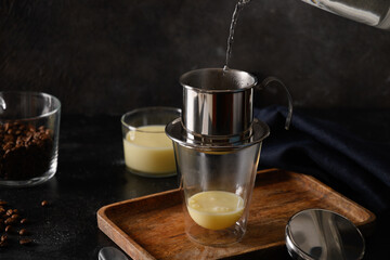 Cooking Vietnamese coffee with sweet condensed milk in glass cup on black background. Close up....