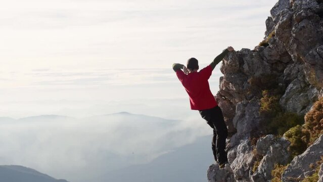 Climber man clinging without a rope to the rock of a mountain making victory gestures after reaching the top and contemplating the sunset on the mountain. Concept of motivation and sport. risk sport.