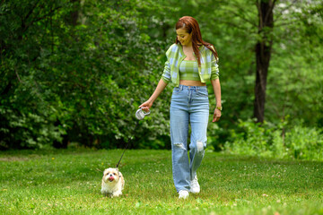 Woman in Green Crop Top Walks Little White Dog in Lush Green Park