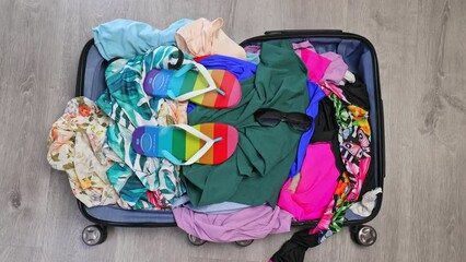 Preparing luggage for summer vacation trip. Someone throws crumpled things and clothes into a suitcase on the floor. Travel concept.