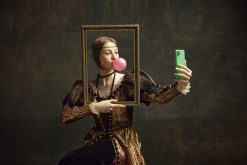 Portrait of pretty young girl, princess with bubble gum, holding picture frame and taking selfie...