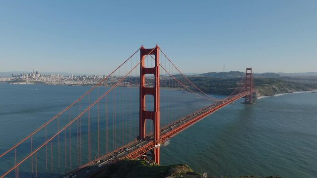 Nice footage of heavy traffic on important thoroughfare. Famous Golden Gate Bridge lit by sun at golden hour. Buildings in city in background. San Francisco, California, USA