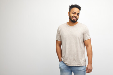 Indoor shot of handsome african american male in t-shirt with pensive expression, smiling and looking happy, isolated over white background with copy space for your promotional text 