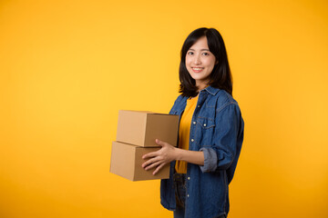 Portrait asian young woman wearing yellow t-shirt and denim shirt holding parcel box isolated on yellow studio background, Delivery courier and shipping service concept.
