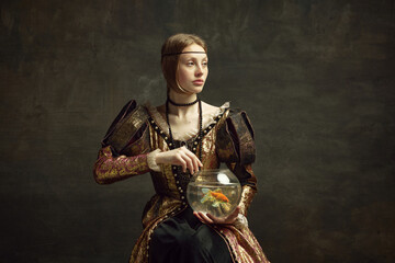 Portrait of royal person, young girl in vintage dress holding large aquarium against dark green background. Concept of history, renaissance art remake, comparison of eras