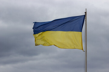 National flag of independence Ukraine on grey cloudy sky. Freedom blue and energizing yellow colors. Stop war in Ukraine