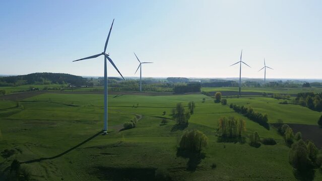 Aerial view of a wind turbine farm in a green landscape. The camera is slowly moving away
