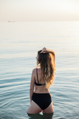a woman in a black swimsuit stands in the water in the sea rest on the beach