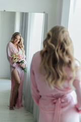 Fototapeta premium a beautiful woman in a pink dress with flowers stands in front of the mirror