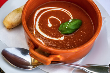 Tomato soup with cream and leaf on plate with spoon and pastry.