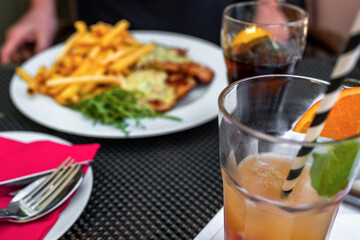 Table with fruity drink and lemonade, plate with cutlery and plate with food.