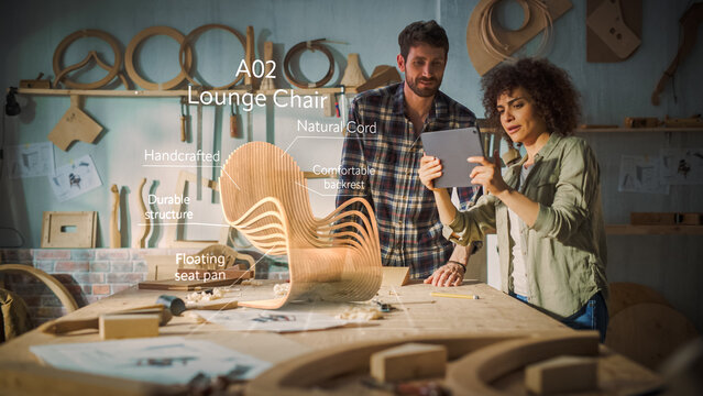Multiethnic Female Furniture Designer Showing to Professional Male Carpenter New Chair Design On Tablet Computer. VFX 3D Hologram Edit Appears on the Work Table With Infographics, Production Info.