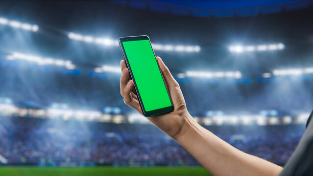 Sport Stadium Championship: Person's Hand Holding Green-Screen Chroma Key Smartphone. Sports Event with Fans Cheering for Favourite Team to Win Championship. Isolated POV Close-up Copyspace Template - Powered by Adobe