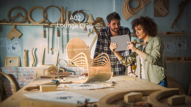 Multiethnic Female Furniture Designer is Showing Professional Male Carpenter New Chair Design On Tablet Computer. VFX 3D Hologram Edit Appears on the Work Table With Measurements for Production.