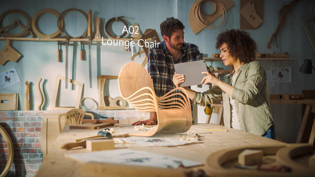 Multiethnic Female Furniture Designer is Showing Professional Male Carpenter New Chair Design On Tablet Computer. VFX 3D Hologram Edit Appears on the Work Table With Infographics, Production Info