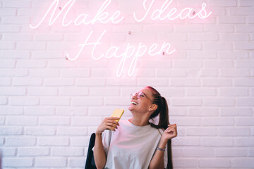 Smiling woman enjoying while sitting near white wall