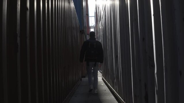 Low shot of a person walking with his back to the camera between containers, misting from the cold of the morning.