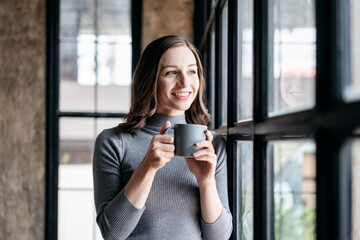 Fototapeta premium Businesswoman cozy lifestyle concept, Businesswoman drinking hot chocolate and standing near window to looking outside for take a break with enjoying while relaxation after working