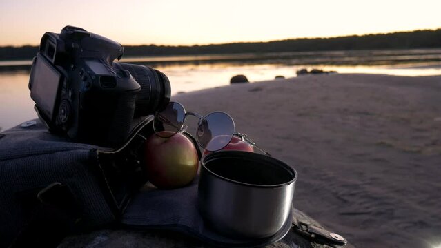 Photographer's bag with 2 apples and coffee. Tourist halt on the stone against the background of the lake and a beautiful sunset.