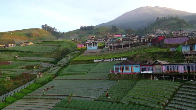 Text "Selamat Datang di Dusun Butuh" or "Welcome to Butuh Village" at the entrance of Nepal Van Java village with view of beautiful rura landscape and peak of Mount Sumbing - 4K Aerial Drone Shot
