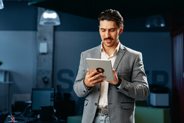 Young successful businessman working on digital tablet while standing in office