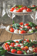 Classic italian salad Insalata Caprese with cherry tomatoes, mini mozarella pearls, basil leaves and balsamic glaze served on a cake stand, vertical