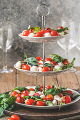 Classic italian salad Insalata Caprese with cherry tomatoes, mini mozarella pearls, basil leaves and balsamic glaze served on a cake stand, vertical