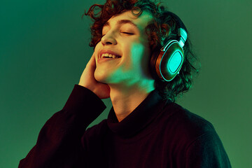 Man portrait in headphones listening to music, dancing and singing with his eyes closed, DJ happiness and smile laughter, hipster teenager lifestyle, portrait green background neon light, copy space