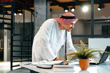 Young muslim businessman in traditional outfit working at the table in office