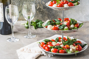 Classic italian salad Insalata Caprese with cherry tomatoes, mini mozarella pearls, basil leaves and balsamic glaze served on a cake stand, gray background