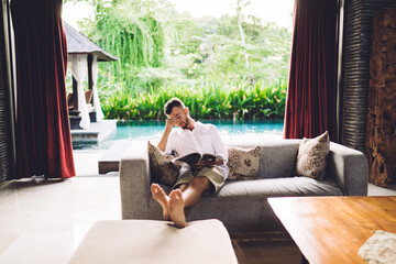 Obraz premium Caucaisan male with journal for reading during weekend leisure feeling tired, young barefoot man in casual wear bored during free time for literature hobby - home spending at house terrace