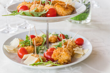 Fried breaded prawns with rocket salad on a porcelain cake stand on a white, elegantly set table
