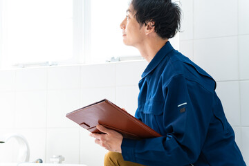 風呂場をチェックする作業着を着た日本人男性 - obrazy, fototapety, plakaty
