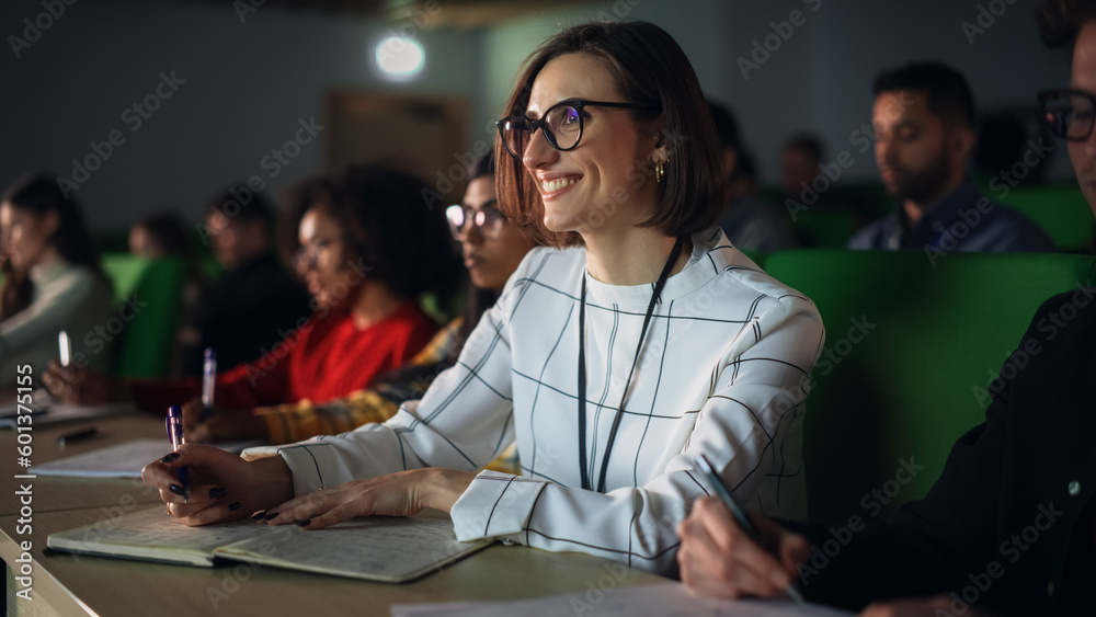 Poster thoughtful beautiful young female studying in university, listening to a lecture in a crowded room w