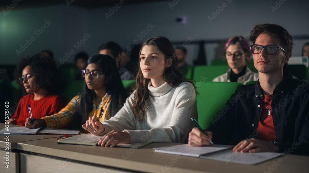 Poster thoughtful beautiful young female studying in university, listening to a lecture in a crowded room w